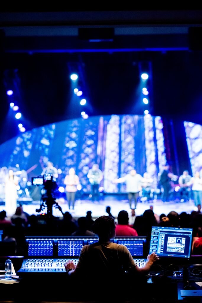 Nosotros, sincro producciones, productora de eventos medellin, alquiler sonido, alquiler pantallas Sound engineer at a live concert, vibrant stage lighting, musical performance.