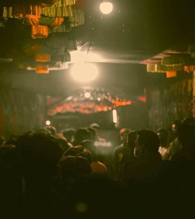 A crowded alleyway at night with people surrounded by dim, moody lighting, enhancing a mysterious atmosphere.